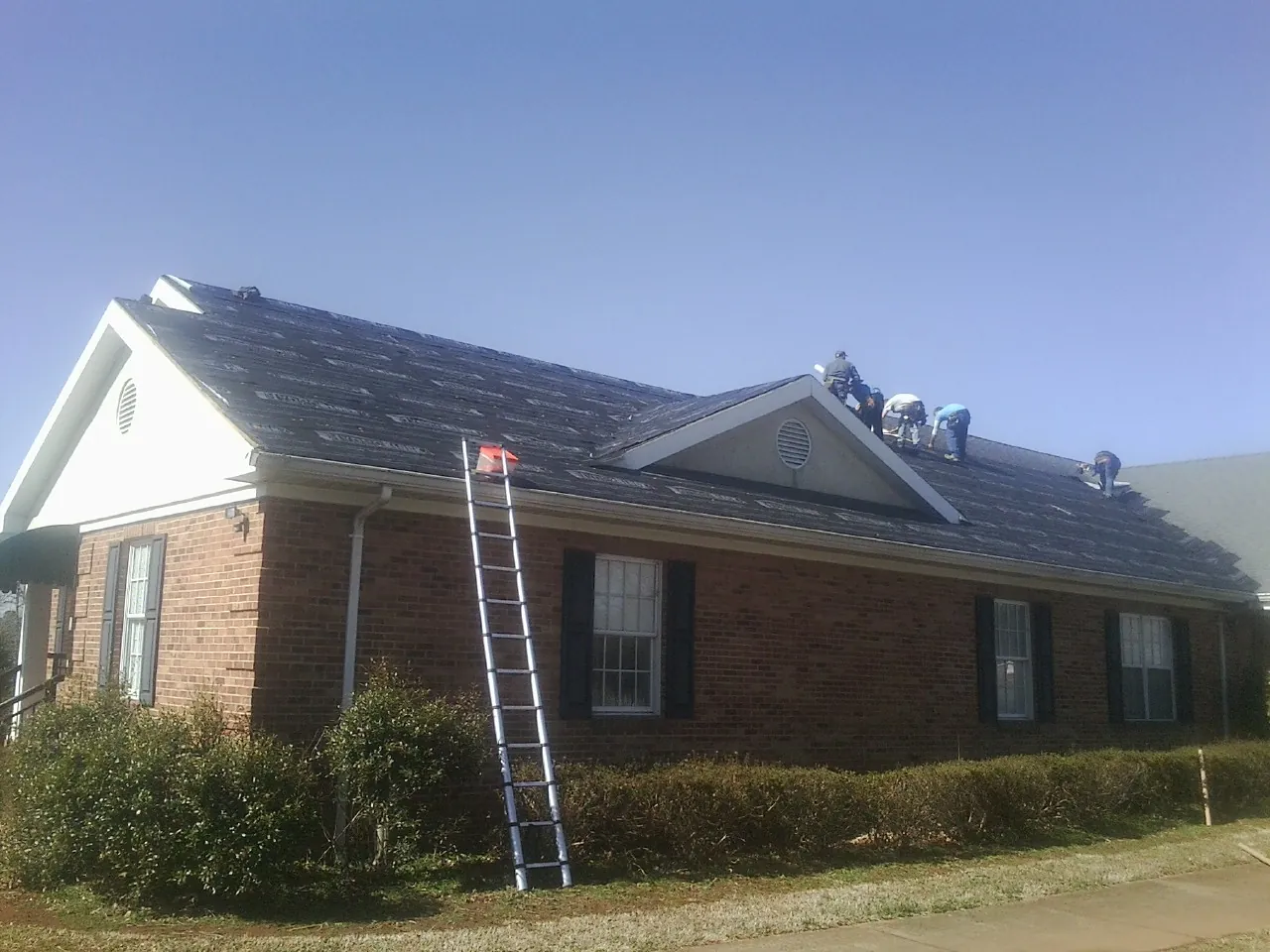 Crew tearing shingles off a brick ranch roof with a ladder set — Metal Roof Repair work by our crew in Fraser