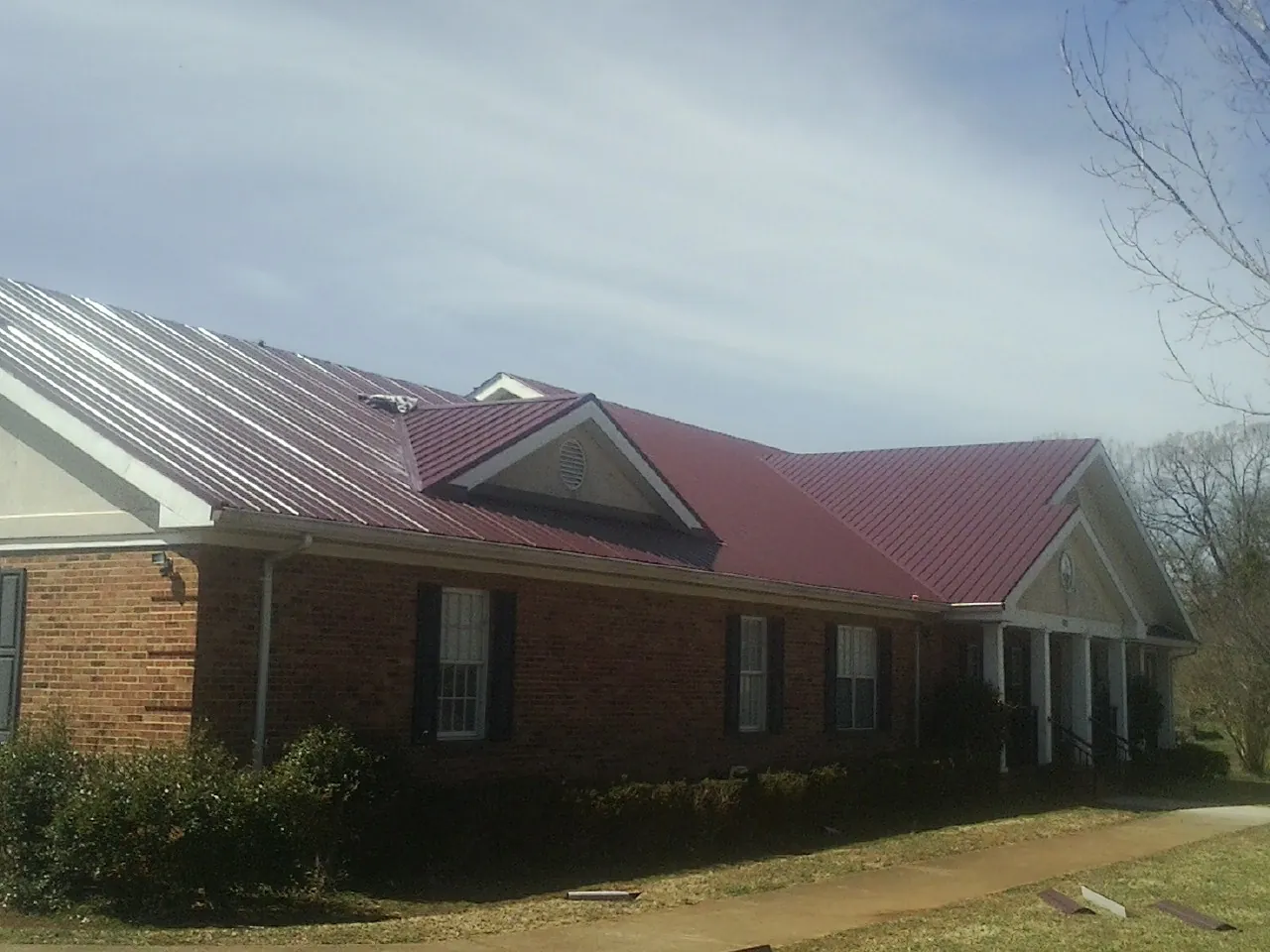 Red metal roof with gabled entries on a long brick building, from a Hail Damage Roof Repair job in Fraser