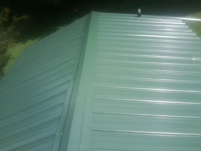 New green metal panels meeting at the ridge of a roof — Flat Roof Repair work by our crew in Fraser