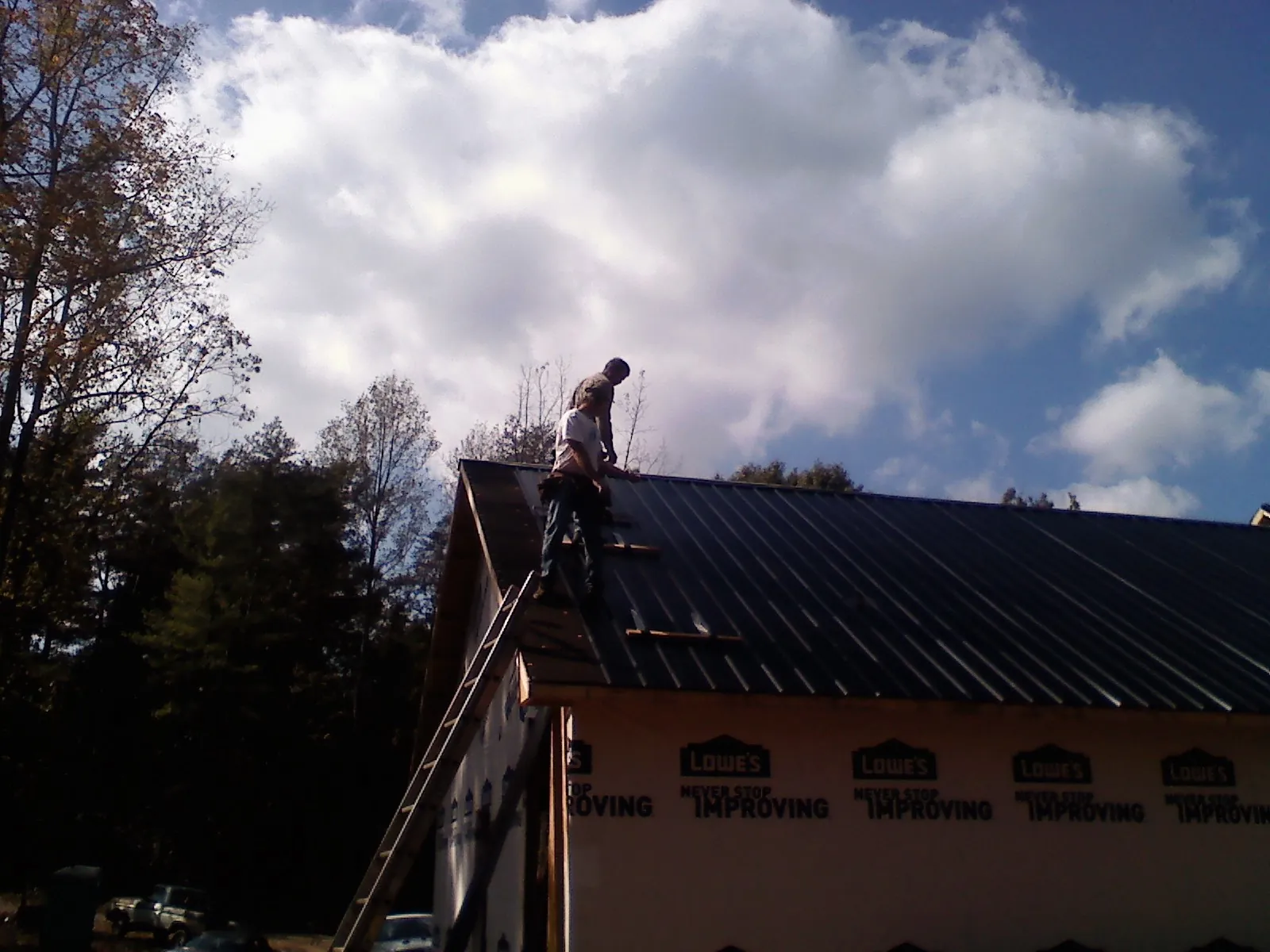 Roofer fastening dark metal panels high against a cloudy sky, from a Roof Inspection job in Fraser